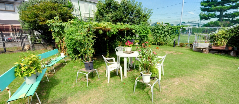 施設の庭園。緑に囲まれたテーブルと椅子、プランターが配置されている。